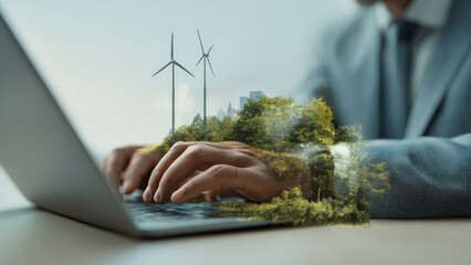 Businessman typing on laptop with wind turbines and forest overlay.