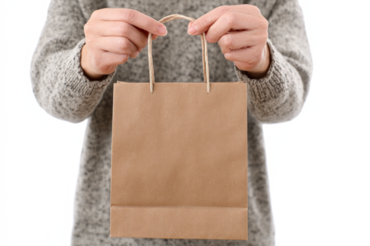 A person in a grey sweater holds a small, plain brown paper gift bag with twisted paper handles.