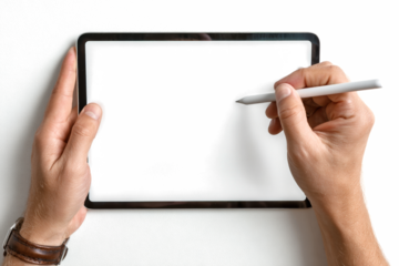 Overhead view of a person's hands holding a modern digital tablet with a blank white screen and a stylus pen.