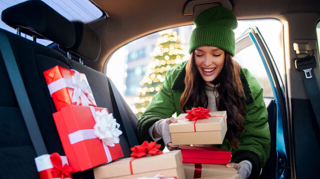 Happy woman delivering Christmas gifts to friends and family, packing Xmas presents to her car, enjoying festive mood and holiday spirit - Powered by Adobe