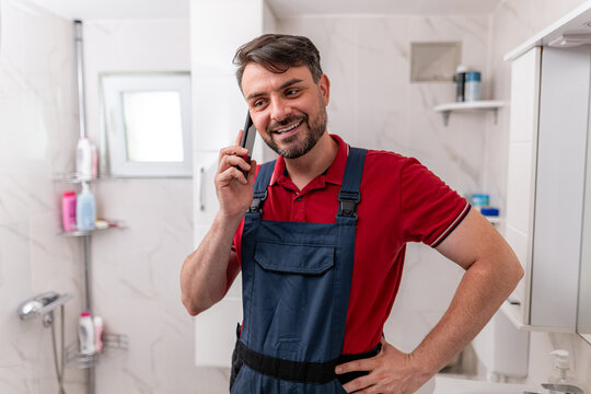 Happy plumber talking on the phone while preparing for bathroom repairs