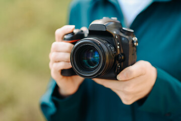 black dslr camera in hands, young caucasian woman photographer in green shirt at work outdoors in sunny summer day