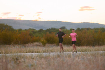 Obraz premium A couple dressed in sportswear runs along a scenic road during an early morning workout, enjoying the fresh air and maintaining a healthy lifestyle