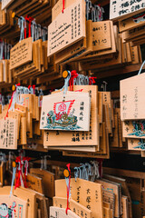 Obraz premium Wooden Ema prayer plaques hanging at a Japanese shrine or temple. Close-up of traditional wooden wishing tablets with calligraphy and red ties.