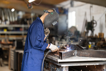 Male welder in protective helmet welds metal part in workshop