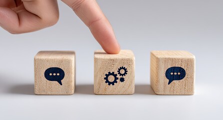 A finger points to a wooden block displaying a gear icon, between two blocks with speech bubble icons
