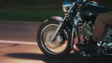 Close up of motorcycle front wheel and engine during evening ride, showing rider boot on footrest, spinning tire, chrome details, and road illuminated by warm streetlights in motion blur - Powered by Adobe