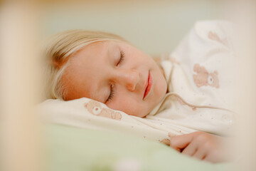 A young girl with long blonde hair is sleeping soundly on her side in a bedroom. She is dressed in a soft pajama outfit and surrounded by a calm atmosphere.