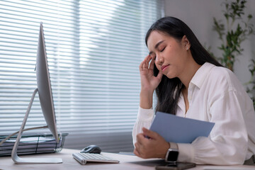 Stressed asian businesswoman having headache while working on computer in office