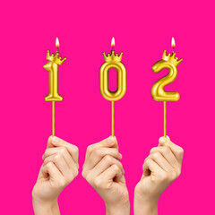 Birthday on a fuchsia background with the number 102 - Hands holding number-shaped candles