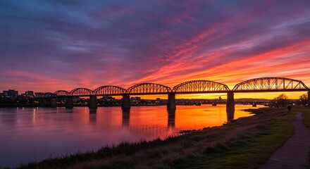 Naklejka premium Bridge silhouette at sunset with colorful sky and water reflection