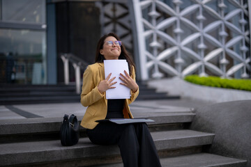 Happy businesswoman holding documents and sitting on stairs outside office building