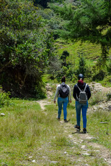 Obraz premium Mother and Teenage Daughter Hiking Together Along Rocky Riverbed Trail Towards Green Rolling Hill, Enjoying Adventure and Ecotourism in Rural Landscape