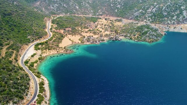 aerial perspective captures the stunning beauty of Cennet Koyu, also known as Paradise Bay, in Turkey. The vibrant turquoise waters of the bay meet the lush green coastline, where a winding road grace