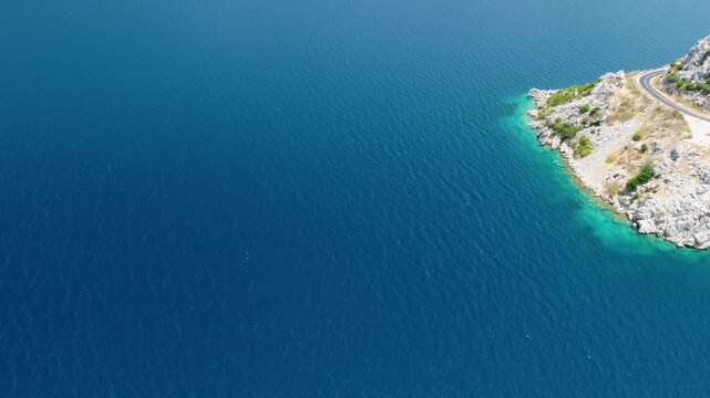 aerial footage captures the beauty of Cennet Koyu Paradise Bay in Bodrum, Turkey. The vibrant turquoise waters meet the rugged, green coastline, featuring a winding coastal road. This serene landscape