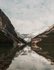 Vertical view of Lake Louise reflecting snow-covered mountains and glacier. Rocky banks, water reflection, cloudy sky.