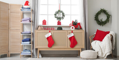 Festive living room with stacks of winter clothes on shelving unit, wooden cabinet and Christmas...