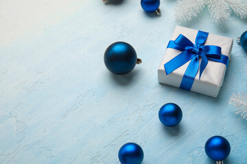 Christmas tree branches with balls and gift box on light blue background