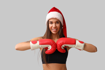 Sporty young woman in Santa hat and boxing gloves on light background