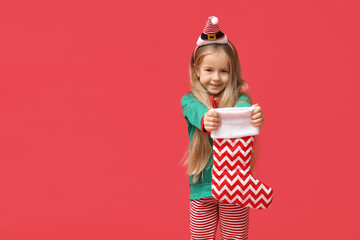 Cute little girl in Christmas elf costume with sock on red background