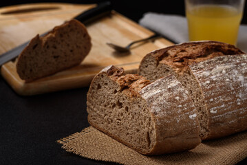 Dark rye sourdough bread sliced on a brown wooden cutting board on a black background