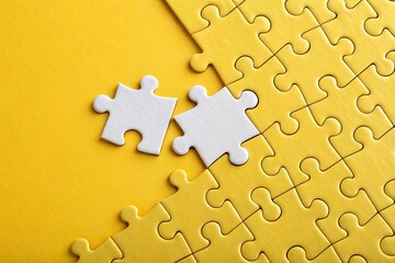 Obraz premium Two white puzzle pieces on a bright yellow background, symbolizing problem-solving and creativity