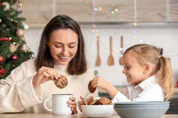 Young mother with her little daughter eating cookies with hot chocolate at home on Christmas eve