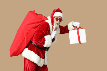 Shocked Santa Claus in sunglasses with bag full of gift boxes on brown background