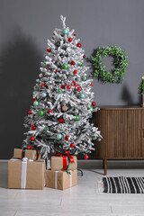 Decorated Christmas tree with gifts and dresser against grey wall
