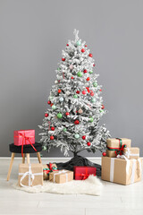 Decorated Christmas tree with gifts and stool against grey wall