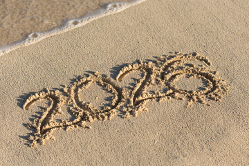 Inscription 2026 on sandy beach with wave's foam. Christmas and New Year celebration