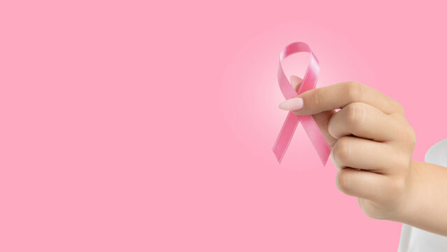 A person holds a pink ribbon symbolizing cancer awareness