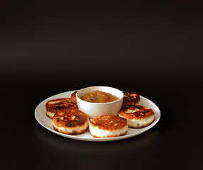 Cheesecakes with raisins and apple jam in a round white plate on a black background.