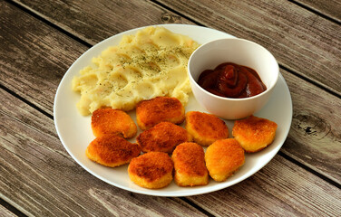 Fresh fried chicken nuggets with mashed potatoes and tomato sauce in a round plate on a wooden table.