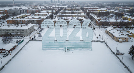 New Year Frozen Display: Aerial view of a large ice sculpture displaying the year 2026, set against a snow-covered cityscape, showcasing a unique winter celebration.