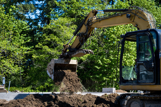 Workman using excavator, heavy construction equipment, to remove dirt to dig new house foundation, earthworks
