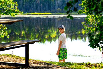 Teen boy at the little forest lake in hot summer day.