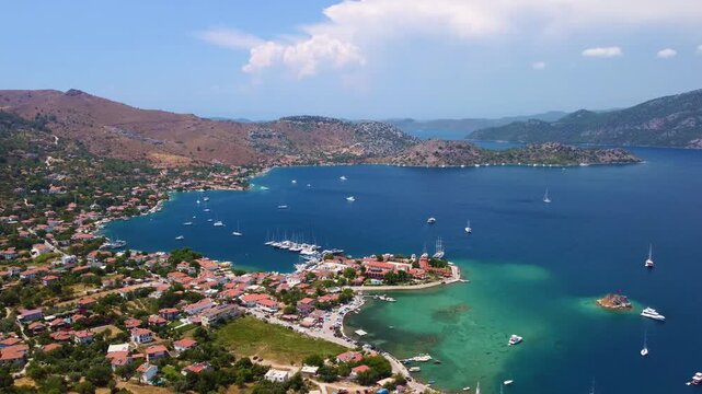 aerial drone footage captures the beauty of Cennet Koyu Paradise Bay in Selimiye, Marmaris, Turkey. This serene coastal landscape showcases crystal clear turquoise waters, lush green hills, and the ch