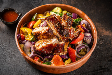 Roasted pork ribs with grilled vegetables in clay bowl