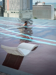 Man swimming in infinity roof top pool. City view at the background.
