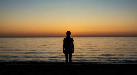 Silhouette of a person at sunset on a tranquil beach, gazing at the vast ocean horizon.
