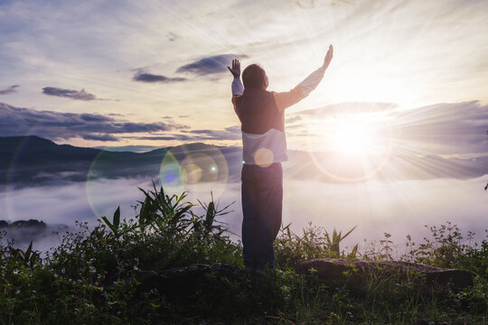 Man prays to God with his hands raised to the sky at the sun rises early morning on mountain misty