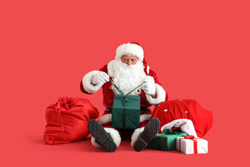 Santa Claus with bags and Christmas gift boxes sitting on red background