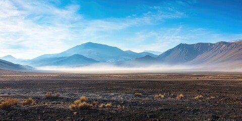 A vast, barren landscape with mountains in the distance, a thin layer of fog or mist in the foreground, and a clear blue sky above.