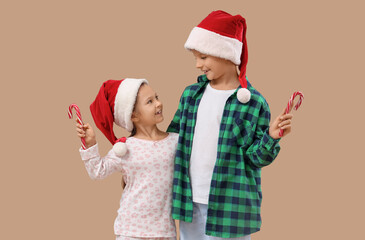 Cute little children in Santa hats with candy canes on beige background