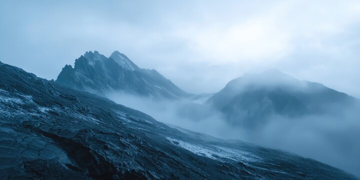 A misty mountain landscape with jagged peaks and a rocky foreground, under a cloudy sky with a muted blue hue.