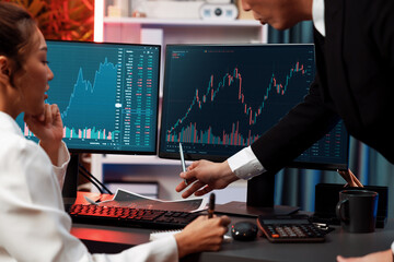 Smiling Asian business traders pointing to dynamic stock exchange data screen profit value online...