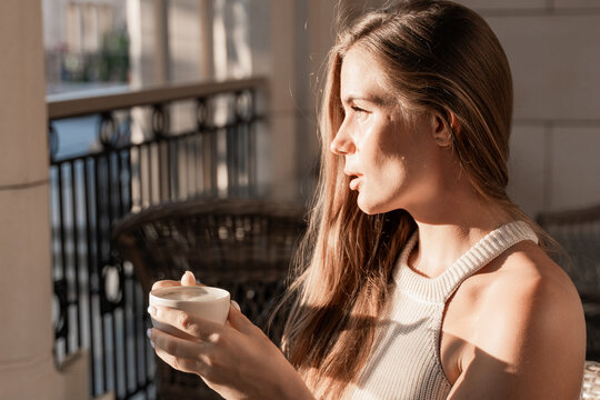 Woman Coffee Window - A woman holding a cup of coffee looks out the window on a sunny day.