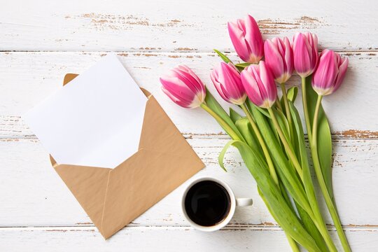 Pink tulips with coffee cup and envelope on white wooden background