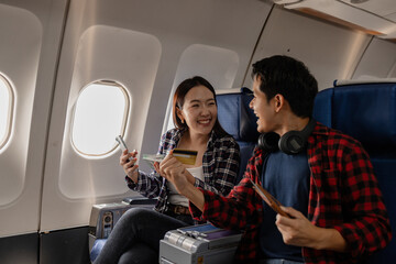 Smiling Asian couple sitting together on an airplane, holding cash, credit cards, and a passport, showing financial readiness and excitement for travel. They look happy and relaxed during the flight.